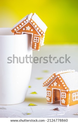 Gingerbread huts and a cup of milk on a white concrete surface with sparkles, close-up view. Christmas celebration concept