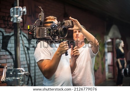 Behind the scenes. Cameraman shooting the film scene with his camera on outdoor set. Photography director in movie filmmaking action