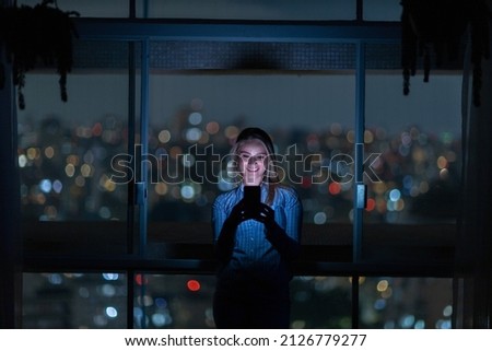 Young woman using a smartphone at night time with city view landscape in the background. High quality photo. Mobile phone, technology, concept. High quality photo
