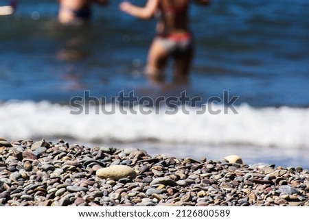 Texture of coastal gravel with unrecognizable people having fun in the sea in the background, concept of lifestyle and fun. Horizontal.