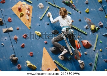 Teenage girl at indoor climbing wall. Kid having fun at bouldering wall. Child learning at climbing class. Sports healthy lifestyle. Youth at climbing summer camp Royalty-Free Stock Photo #2126801996