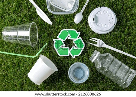 environment, sustainability and ecology concept - close up of green recycling sign and plastic waste on grass