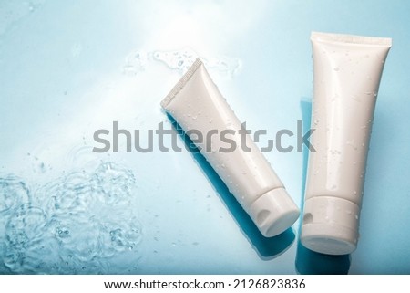 White cosmetic products in tubes on color blue background with water drops. Mock up skincare cosmetic packages on water surface. Natural moisturizing water balance cosmetics product.