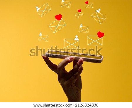 female hand holds a smartphone with flying out letters on a yellow background. Social media addiction, receiving correspondence and appraisal. 