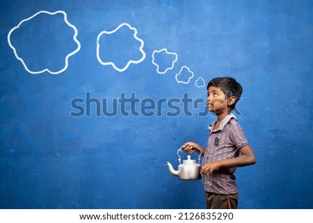 poor tea selling kid thinking by holding tea glass and container in hand with cloud doodle drawing on blue background - cocept of poverty, child labour and imagination Royalty-Free Stock Photo #2126835290