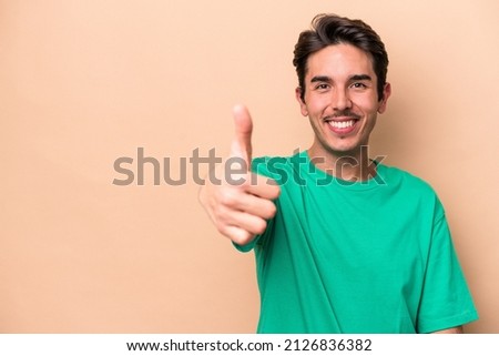 Young caucasian man isolated on beige background smiling and raising thumb up