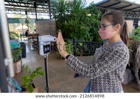 An Asian woman measures her temperature with a digital thermometer before entering a restaurant. according to virus prevention measures.