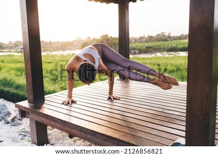 Strong female standing on hands training body balance during free time for exercising in Indonesia, Caucasian woman in sportswear have yoga practice at terrace near rice fields in Thailand
