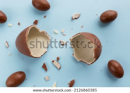 Two halves of a broken chocolate egg for children a chocolate egg with small eggs around on a blue background. Copy space in the middle. Easter card, top view. Royalty-Free Stock Photo #2126860385