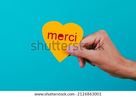 closeup of a man with a yellow heart in his hand with the text thank you written in french, on a blue background