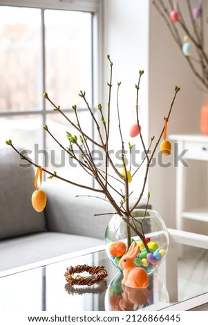 Vase with tree branches and Easter eggs on glass table in living room