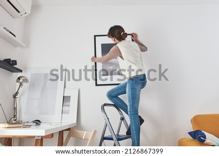 Girl child teenager on the ladder hanging pictures and photos on the shelf and wall at home.