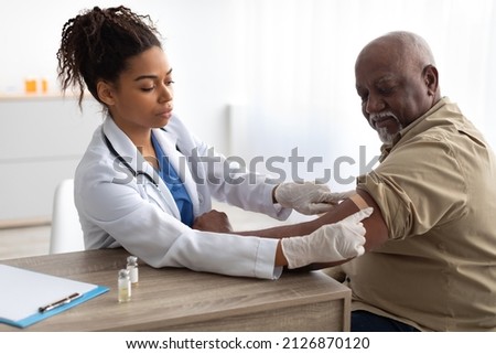 Vaccination Concept. Senior Man Getting Vaccinated Against Flu Or Corona Virus With Antiviral Vaccine, Female Doctor Putting Applying Sticking Adhesive Bandage On Arm After Injection In Hospital Royalty-Free Stock Photo #2126870120
