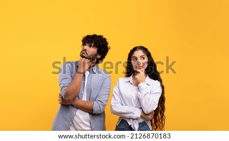 Portrait of pensive indian man and woman thinking and looking up at free space, touching chin, standing over yellow studio background. Thoughtful couple making decision Royalty-Free Stock Photo #2126870183