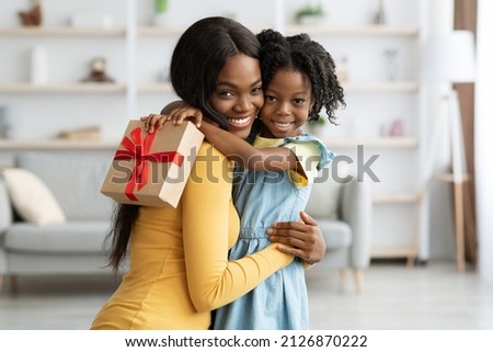 Mother's Day Concept. Adorable Female Child Holding Gift And Embracing Mom, Portrait Of Happy African American Mommy And Her Cute Little Daugher Bonding Together At Home, Copy Space Royalty-Free Stock Photo #2126870222
