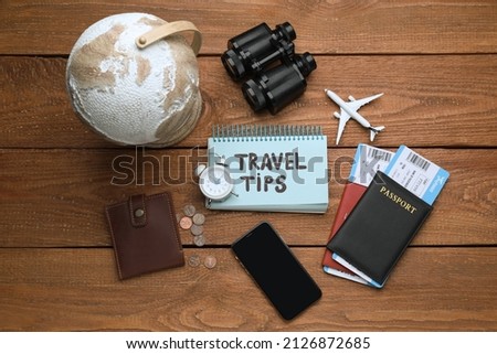 Notebook with phrase Travel Tips, smartphone and tourist items on wooden table, flat lay