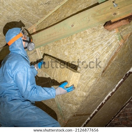 Attic renovation and insulation concept. Worker in uniform installing thermal roof insulation layer using mineral wool panels