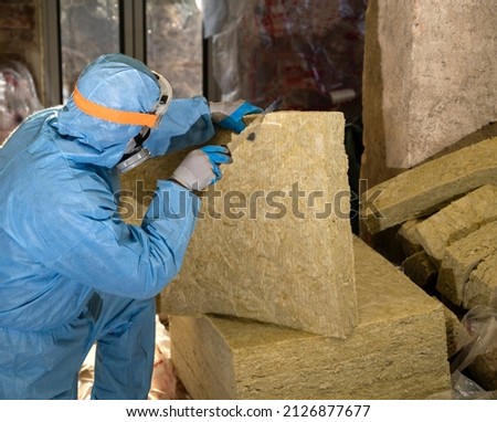 Attic renovation and insulation concept. Worker in uniform cutting  mineral wool panels