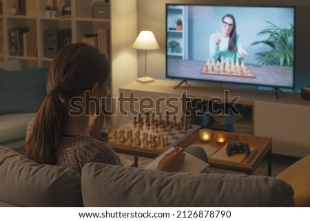 Woman sitting on the sofa and learning how to play chess, she is watching a TV show