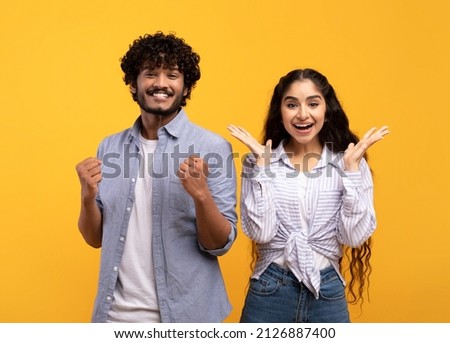 Wow. Overjoyed indian spouses gesturing in amazement looking at camera over yellow studio background. Emotional surprised couple gesturing yes