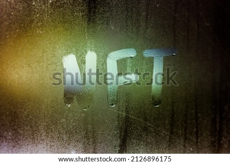 the word NFT - non-fungible token handwritten on foggy window glass at night.