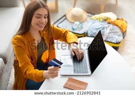 Cheery young lady using credit card and laptop pc with mockup for online travel agency website, booking abroad trip, making hotel reservation on web from home, free space Royalty-Free Stock Photo #2126902841