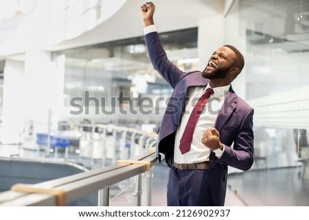 Cheerful african american young businessman celebrating success, handsome black manager in suit and tie raising hands up and screaming, office building interior, panorama with copy space Royalty-Free Stock Photo #2126902937