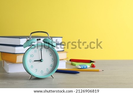 Turquoise alarm clock and different stationery on white wooden table against yellow background, space for text. School time