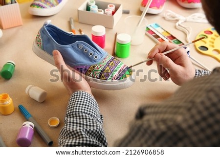 Man painting on sneaker at table, closeup. Customized shoes Royalty-Free Stock Photo #2126906858
