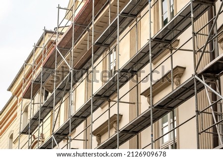 Scaffolding on a generic old tenement house, renovated historical building facade detail, closeup, nobody. Restoration industry, old architecture, real estate renovation simple concept, no people Royalty-Free Stock Photo #2126909678