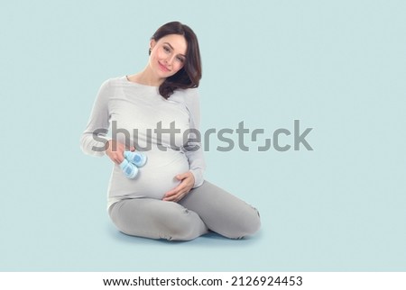 Pregnant Woman touching her belly. Pregnant middle aged mother's hands caressing her tummy. Healthy Pregnancy concept, Sitting Gravid female on blue background, full length portrait Royalty-Free Stock Photo #2126924453