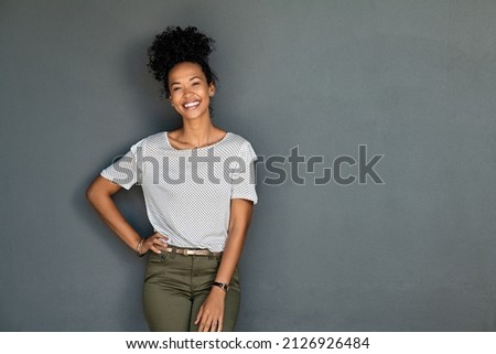 Portrait of young african american woman standing with hands on waist and looking at camera. Confident stylish black girl standing against grey background. Happy afro girl smiling with copy space. Royalty-Free Stock Photo #2126926484