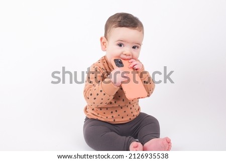 Adorable baby boy wearing animal print sweater sitting on white background holding a smartphone and watching streaming videos or cartoons. 
