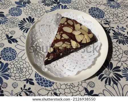 Chocolate brownie topped with almonds, on a white plate, floral patterned cloth.