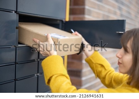 Young woman getting parcel from cell of automatic post terminal outdoors. Concept of contactless and smart delivery. Idea of modern shipping and logistics. Woman wearing yellow sweater Royalty-Free Stock Photo #2126941631