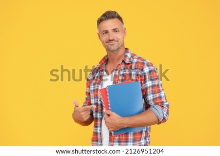 Happy man student pointing finger at books yellow background, education
