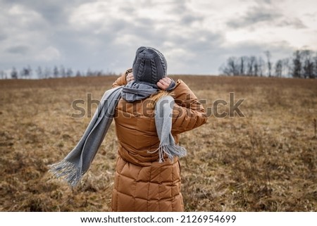 Wind and cold weather. Woman wearing coat, scarf and knit hat outdoors. Female person walks in nature Royalty-Free Stock Photo #2126954699