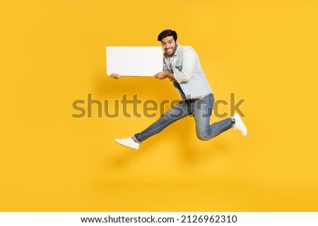 Young man jumping and showing blank white billboard isolated on yellow background