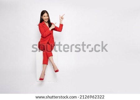 Young Asian businesswoman in red suit sitting and pointing to empty copy space isolated on white background