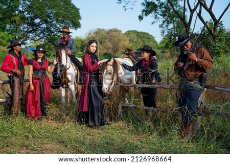 Group of cowboy and cowgirl stay near fence in grasses field and they also bring horse beside of them.