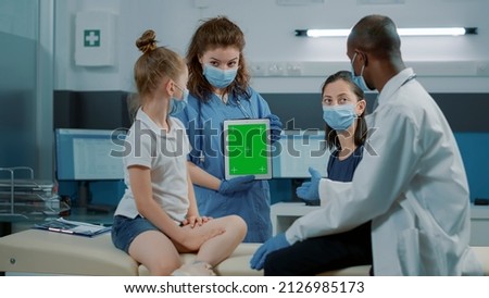 Woman nurse analyzing digital tablet with green screen and doctor explains diagnosis. Assistant holding chroma key background with isolated mockup template and blank copy space during pandemic.