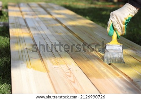 a gloved hand with a brush applies impregnation to wooden boards. protective coating Royalty-Free Stock Photo #2126990726