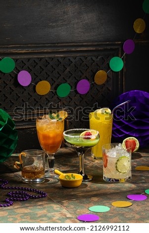 Alcoholic beverage cocktails, purple, green and gold Mardi Gras beads, masks decoration on dark rustic background, festive holiday concept