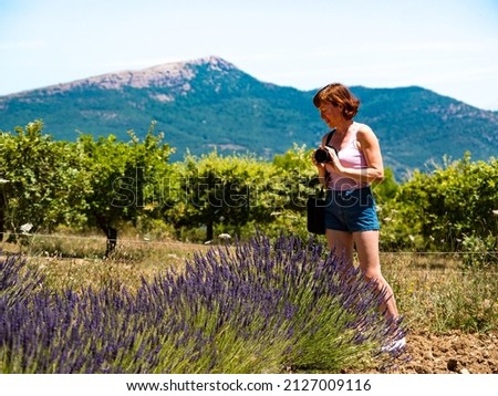 Mature tourist woman with camera taking travel photo from Provence landscape with purple lavender fields, France