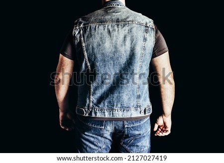 Back view photo of man in jeans shirt and denim biker vest standing on black background. Royalty-Free Stock Photo #2127027419