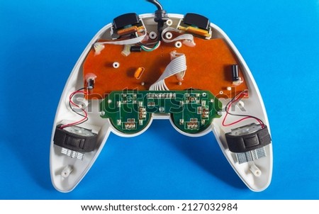 Photo of classic disassembled wired modern silver colored game pad controller laying on blue background.