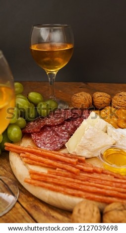 Snacks for wine. Cheese and meat plate. Sausages, cheese, nuts, grapes, crackers on wooden background. Vertical photo