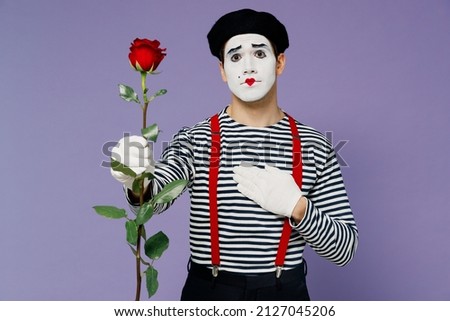 Charismatic sweet romantic young mime man with white face mask wears striped shirt beret hold hand on chest giving rose flower to you isolated on plain pastel light violet background studio portrait