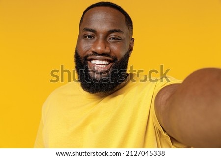Close up young fun smiling happy black man 20s wearing bright casual t-shirt doing selfie shot pov on mobile phone isolated on plain yellow color background studio portrait. People lifestyle concept