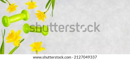 Spring fitness banner. Levitation of green dumbbells and daffodils on a gray concrete background with copy space. 